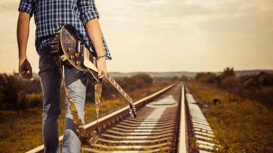 man-holding-electric-guitar-walking-down-train-tracks.jpg